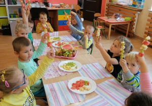 dzieci trzymają w dłoniach gotowe szaszłyki owocowe