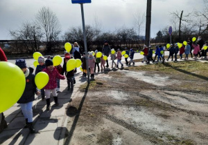 dzieci z zielonymi balonikami spacerują ul. Szkolną