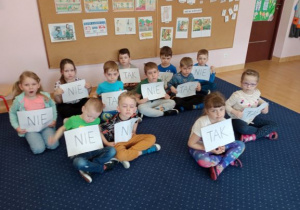 dzieci siedząc na dywanie biorą udział w quizie wiedzy trzymając kartki z odpowiedziami