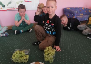 chłopiec trzyma w ręku zielony kiść winogron