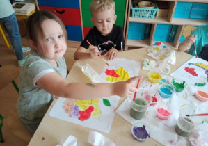 dzieci przy stolikach malują owoce farbami