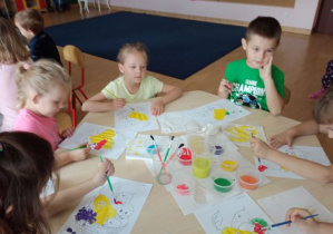 dzieci przy stolikach malują owoce farbami