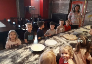 dzieci przygotowują się do formowania ciasta na pizzę
