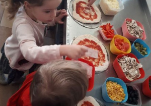 dzieci układają składniki na swoich pizzach