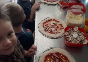 dzieci układają składniki na swoich pizzach