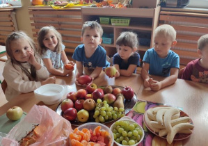 dzieci siedzą przy stole pełnym owoców