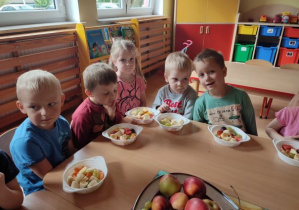 dzieci siedzą przy stole i mają w miseczkach przygotowane owoce do nabijania na patyczki
