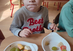 chłopiec siedzi przy stole i wybiera owoce