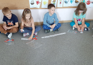 dzieci siedzą na dywanie i układają kartoniki z liczbami.