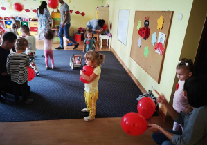 Dzieci i rodzice trzymają czerwone balony w ręku.