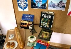 Na stoliku leżą książki i jedzenie związane z Francją.