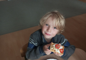 Chłopiec trzyma w ręku gofra z bitą śmietaną i owocami.