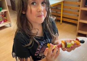 Dziewczynka trzyma szaszłyk owocowy.