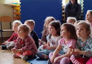 Dzieci siedzą na dywanie i oglądają występ