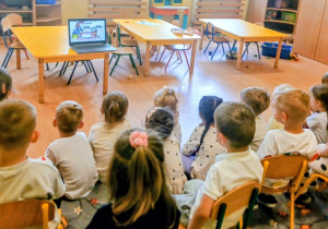Dzieci siedzą i oglądają bajkę edukacyjną.