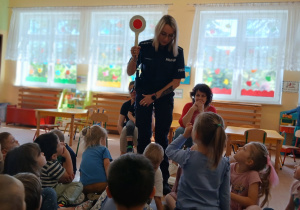 Pani policjantka prowadzi pogadankę dla dzieci i trzyma lizak policyjny.