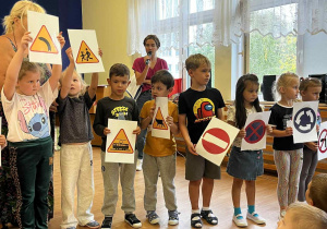 Chłopcy i dziewczynki stoją i trzymają symbole znaków drogowych.