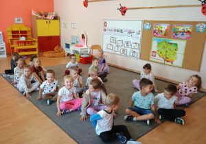 Przedszkolaki siedzą na dywanie.