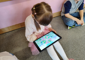 Dziewczynka siedzi i gra na tablecie.