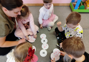 Dzieci siedzą na dywanie i rozwiązują działania matematyczne.