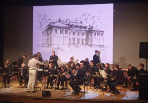 Muzycy z orkiestry siedzą na scenie.