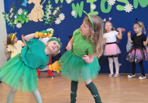 Dziewczynki w stroju żabek tańczą na scenie.