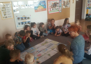 Przedszkolaki siedzą w kręgu na dywanie.
