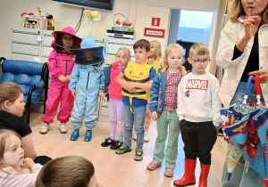 Dzieci w strojach pszczelarza stoją obo chłopca przebranego za pszczołę.