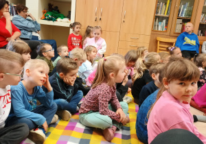 Przedszkolaki siedzą na kolorowym dywanie.