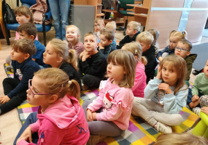 Przedszkolaki siedzą na kolorowym kocu.