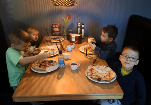 Mali chłopcy jedzą pizzę przy stoliku.