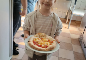Uśmiechnięta dziewczynka trzyma pizzę na talerzyku.