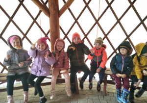 Przedszkolaki siedzą na ławeczce.