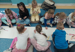Przedszkolaki siedzą na podłodze.