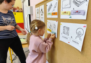 Dziewczynka przypina do korkowej tablicy karteczki z napisami.