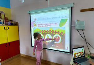 Dziewczynka wskazuje palcem na obrazek wyświetlany na ekranie.