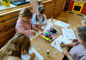Dzieci siedzą przy stoliku i wykonują kartę pracy.