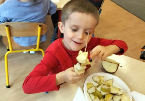 Mały chłopiec nakłada kawałki owoców na patyczek do szaszłyków.