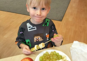 Mały przedszkolak nakłada kawałki owoców na patyczek do szaszłyków.