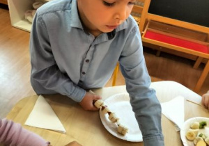 Chłopiec kładzie owocowy szaszłyk na talerzu.