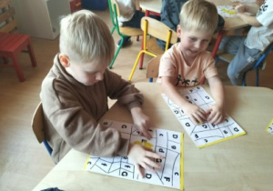 Chłopcy wyklejają plasteliną sylwetę litery E.