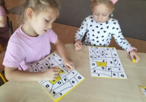 Dziewczynki przy stoliku wyklejają plasteliną kartę pracy.