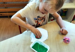 Dziewczynka odciska stempel z jabłka na kartonie.