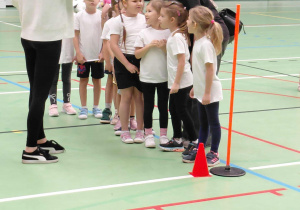 Przedszkolaki stoją na boisku hali sportowej.