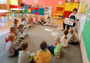 Dzieci siedzą w kręgu na dywanie.