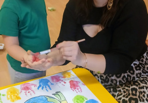 Pani maluje rękę dziecka farbą.