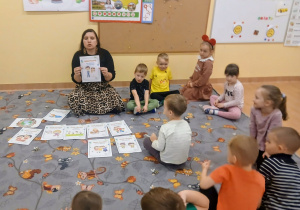 Dzieci siedzą na dywanie i słuchają Pani.