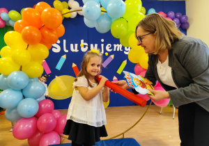 Pani dyrektor kładzie ołówek na ramieniu dziewczynki.