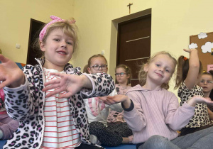 Dzieci siedzą i ruszają rękoma w rytm muzyki.