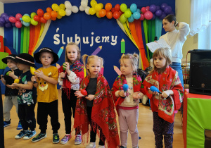 Dzieci w strojach ludowych grają na instrumentach.